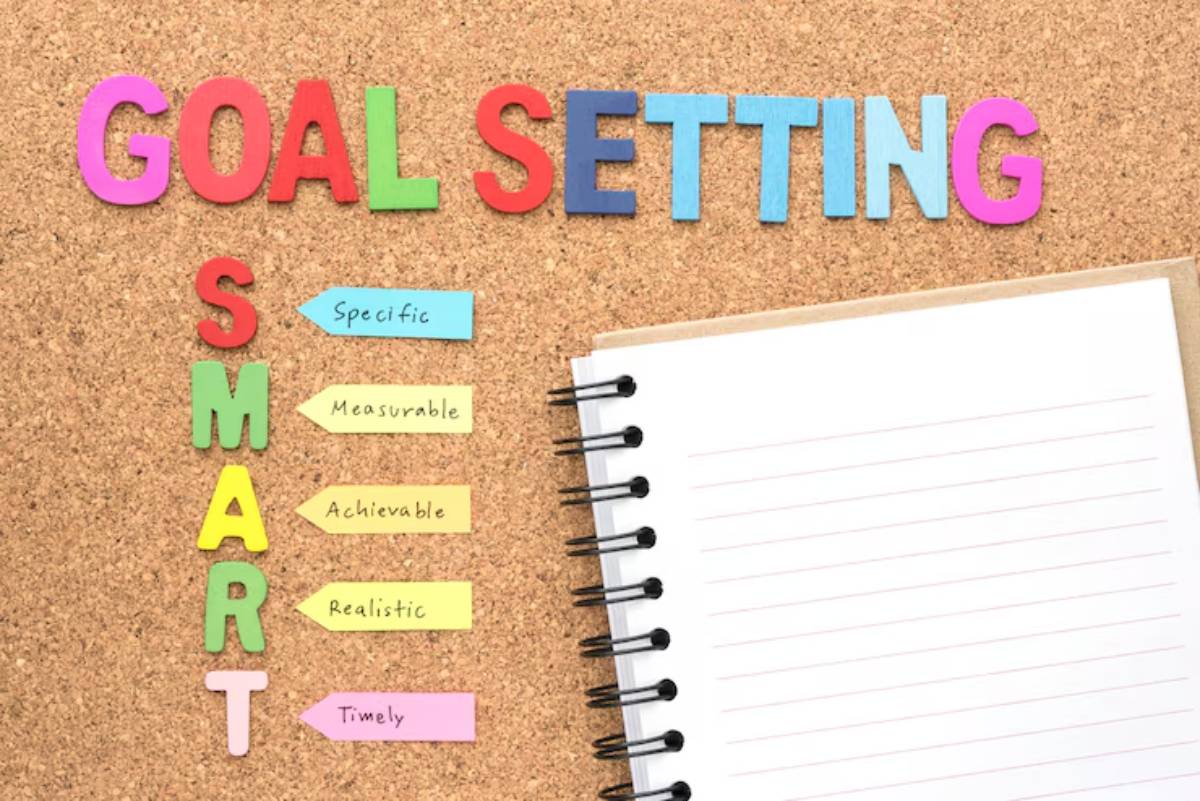 Colorful letters spell 'GOAL SETTING' on a corkboard, listing the SMART criteria: Specific, Measurable, Achievable, Realistic, Timely.