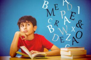 A child in a red shirt sits at a table with an open book, surrounded by floating letters against a blue background.