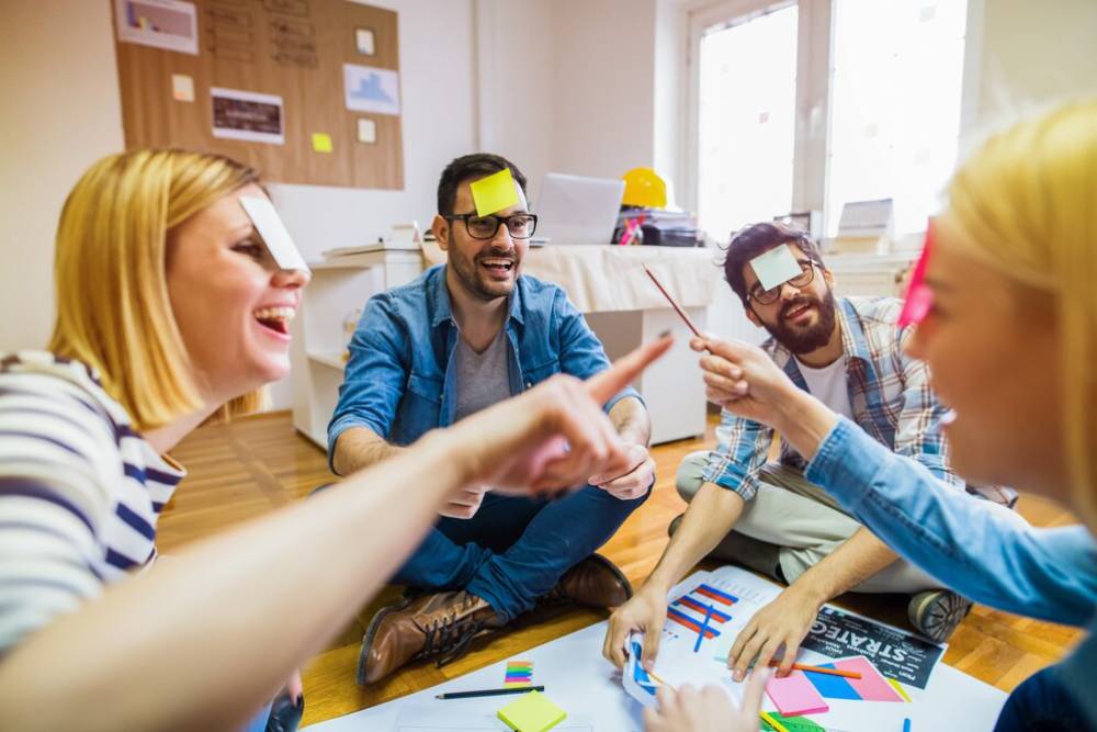 A group of young adults collaborate around a large sheet of paper with colorful sticky notes, engaged in a brainstorming session.