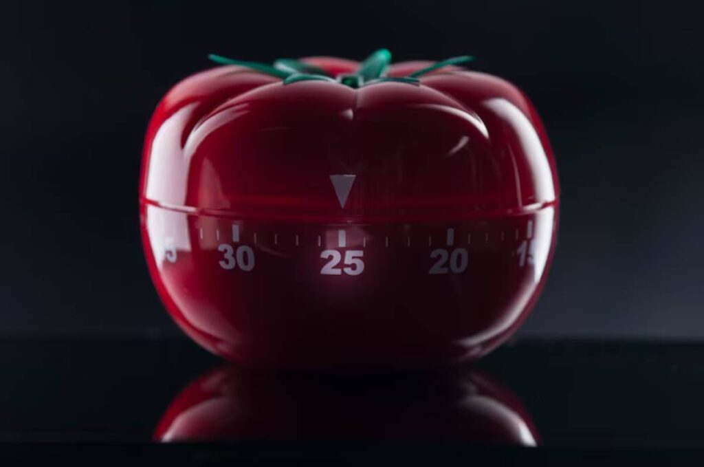 A red tomato-shaped kitchen timer displaying the number 25, against a dark background, reflecting light.