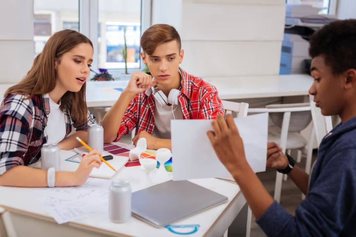 A group of young people engaged in a creative brainstorming session around a table filled with colors, papers, and gadgets.