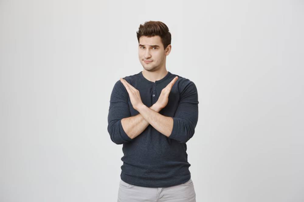 A man wearing a navy long-sleeve shirt crosses his arms in front of his chest, standing against a plain white background.