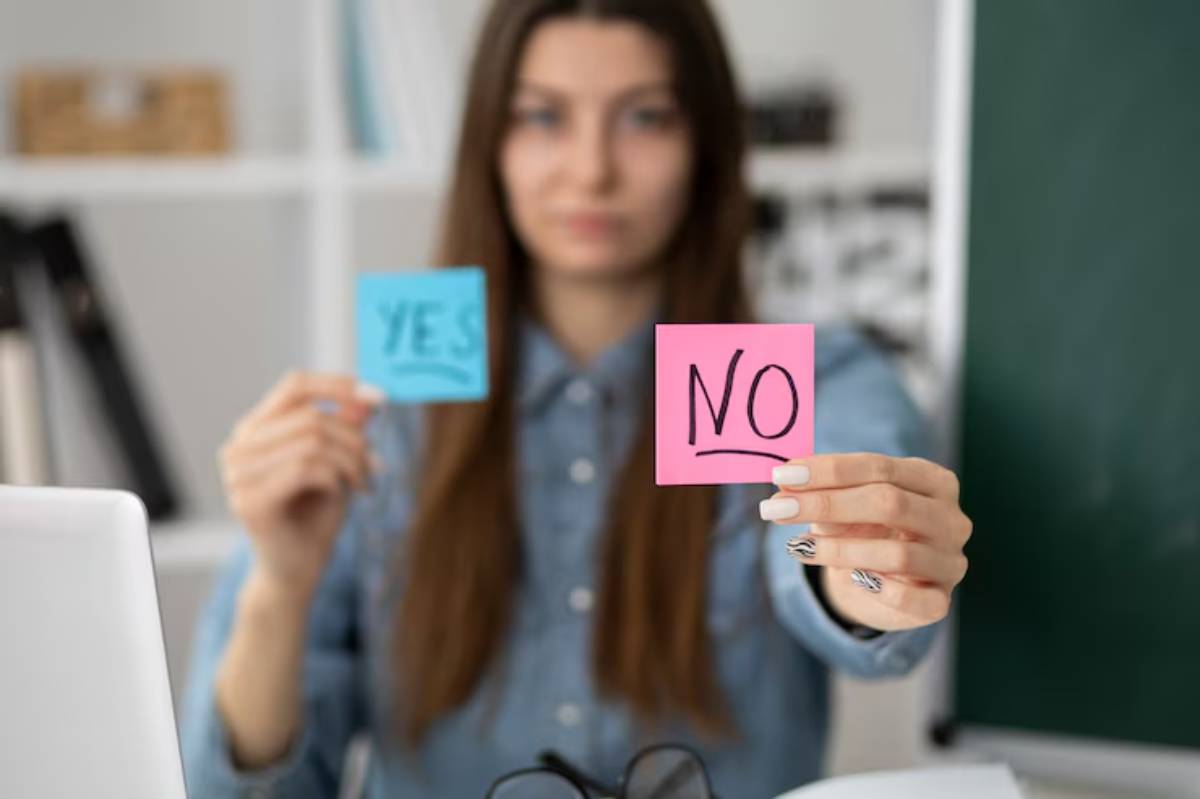 A person holds up two sticky notes, one blue with 'YES' and one pink with 'NO,' in a bright office setting.