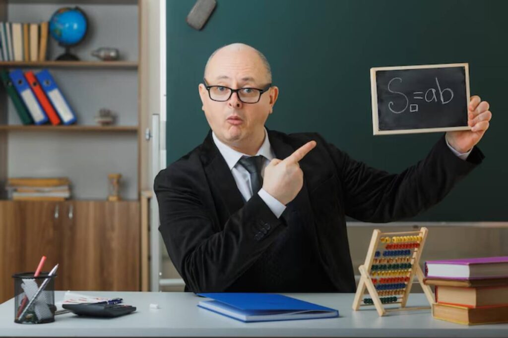 A teacher in a suit points to a chalkboard showing the formula S=ab, with books and an abacus on the desk.