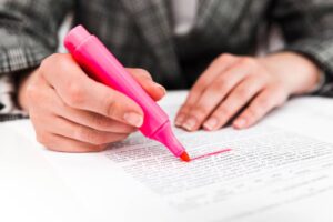 A person highlights text on a paper with a bright pink highlighter, focused on important information. Their hand is visible above the paper.